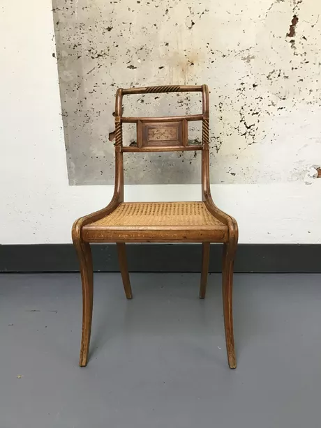 Deze kwartierstoel is van beukenhout gemaakt en heeft een rieten zitting en gesneden rug met een bord waarin een fijn bladmotief van messing is ingelegd.