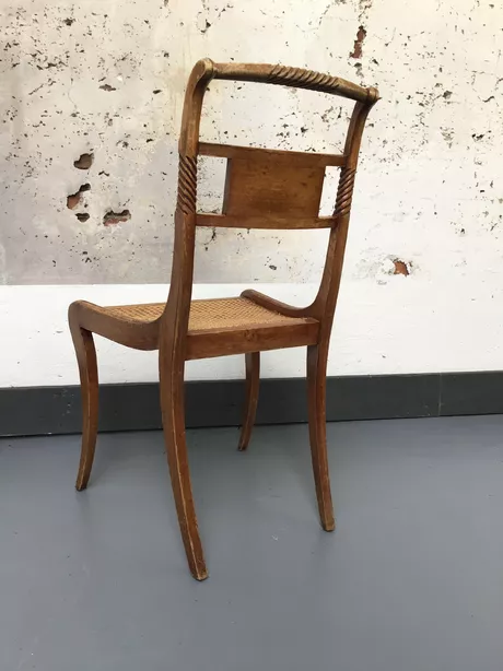 Deze kwartierstoel is van beukenhout gemaakt en heeft een rieten zitting en gesneden rug met een bord waarin een fijn bladmotief van messing is ingelegd.