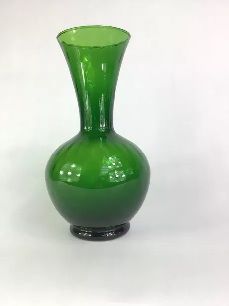 Groene Glazen Vaas Jaren Vijftig Deze prachtige groene vaas uit de jaren '50 heeft een licht geribbeld oppervlak wat het object een unieke textuur en lichtreflectie geeft. De vaas heeft een afgeronde lip (rolled rim). Puntgaaf en onbeschadigd.