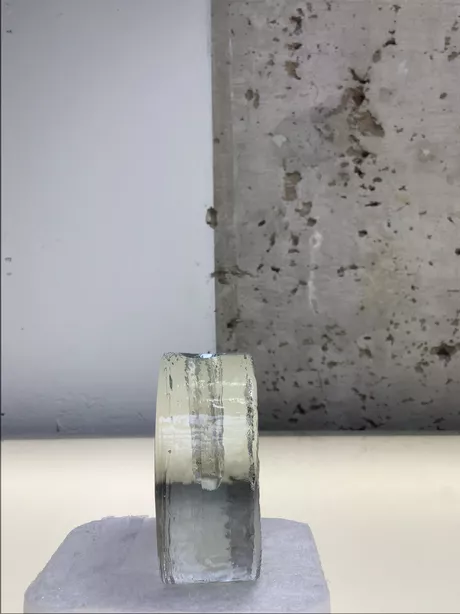 Deze solifleur naar een ontwerp van Heiner Deusterhaus uit de zeventiger jaren, is gemaakt van transparant glas en heeft aan een zijde een bloemmotief glad gesneden op een ruwe achtergrond.