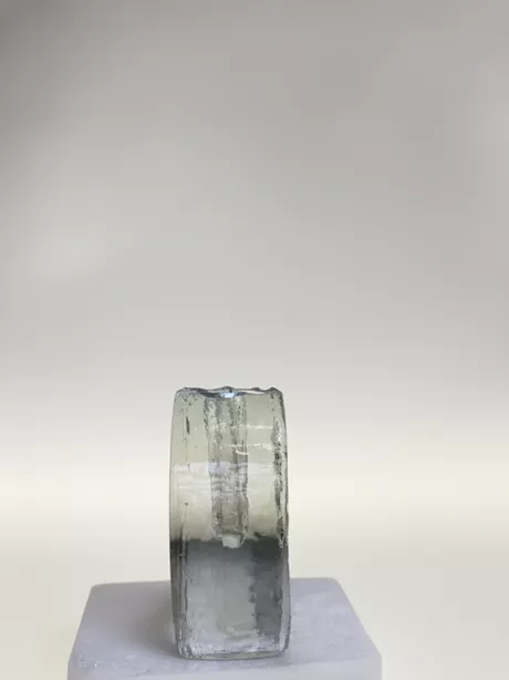 Deze solifleur naar een ontwerp van Heiner Deusterhaus uit de zeventiger jaren, is gemaakt van transparant glas en heeft aan een zijde een bloemmotief glad gesneden op een ruwe achtergrond.