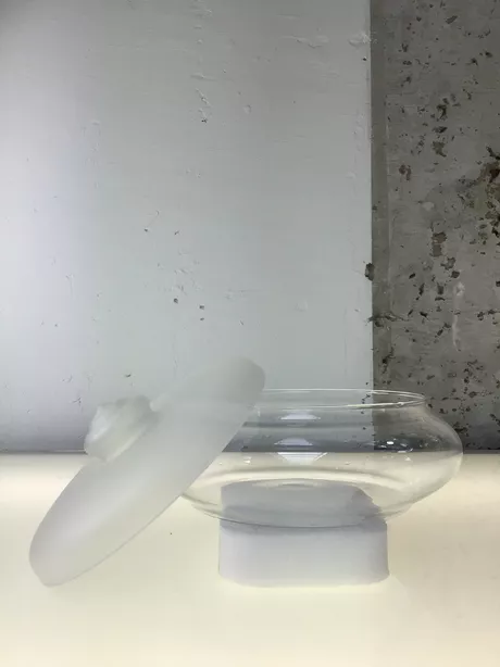 Dit is de bekende Leerdam-bonbonnière/koekdoos van Jacques Boon: helder, geperst of geblazen glas met een gesatineerde (matte) deksel; ontwerp 1934 (modelreeks o.a. VS4053) en decennialang in productie tot ver na de oorlog.